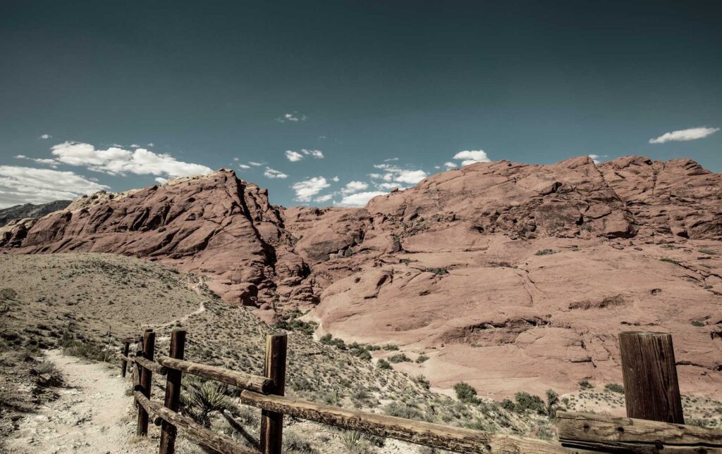 Rocky desert landscape with a wooden fence under a partly cloudy sky.